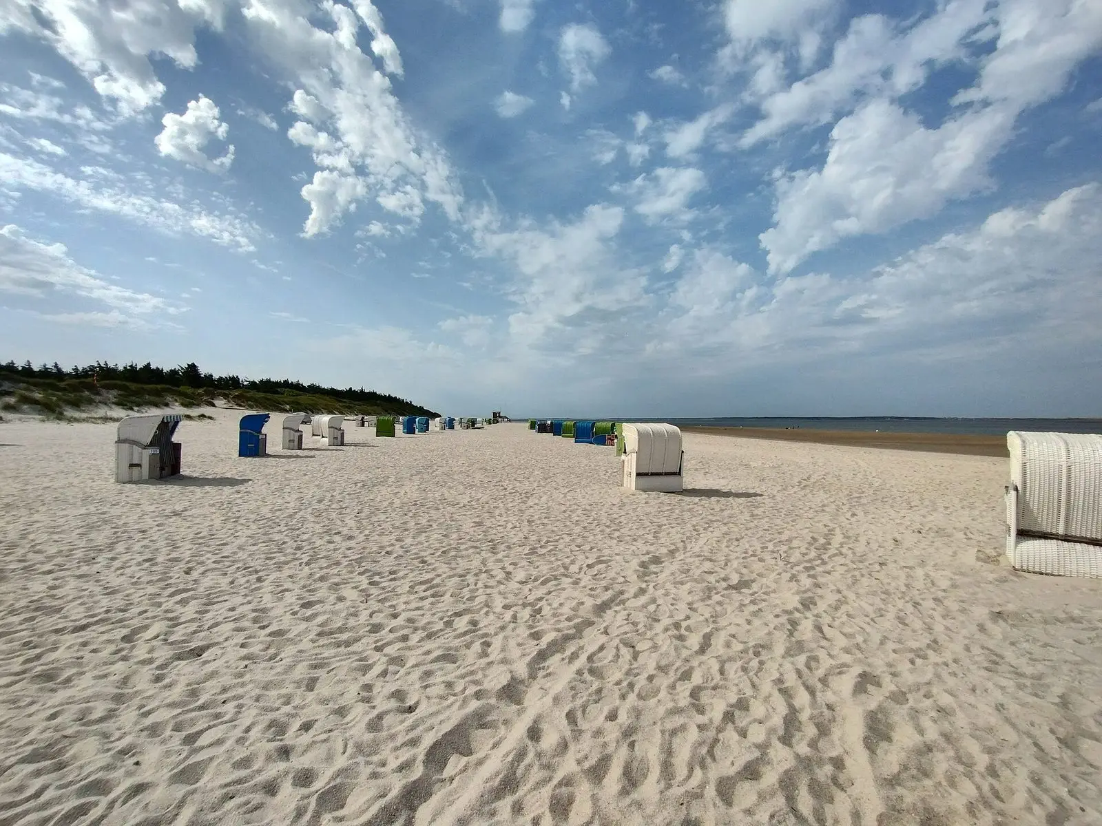 Breiter Sandstrand von Utersum mit Strandkörben unter Federwolken