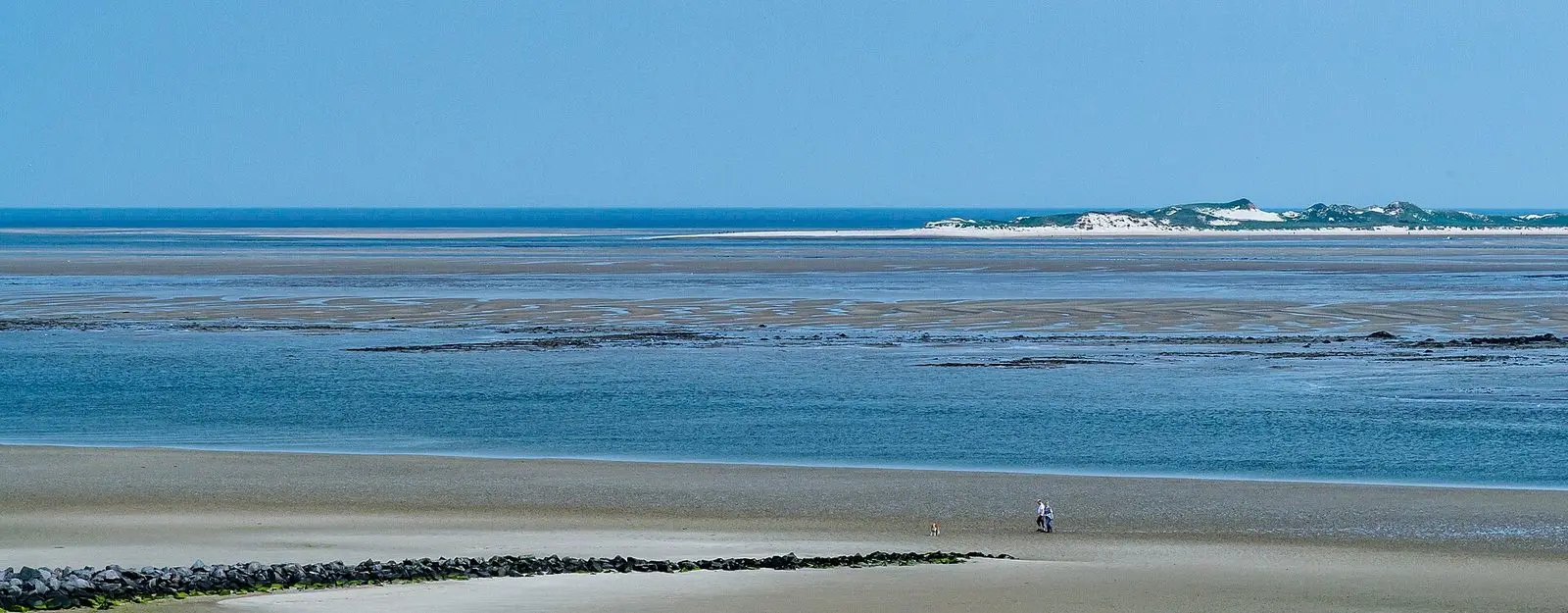 Weiter Blick vom Strand bei Utersum über das Wattenmeer nach Amrum, klein ein Paar mit Hund