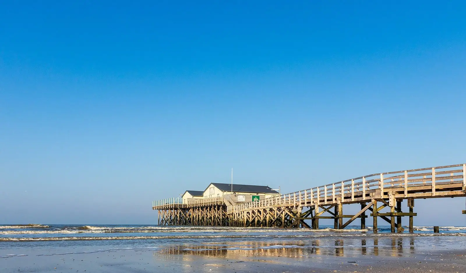 Langer Holzsteg zu einem Pfahlbau im Wasser bei Sankt Peter-Ording unter blauem Himmel